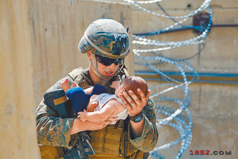 阿富汗喀布尔国际机场内，一名美军陆战队士兵抱着一名婴儿，等候婴儿母亲到来。